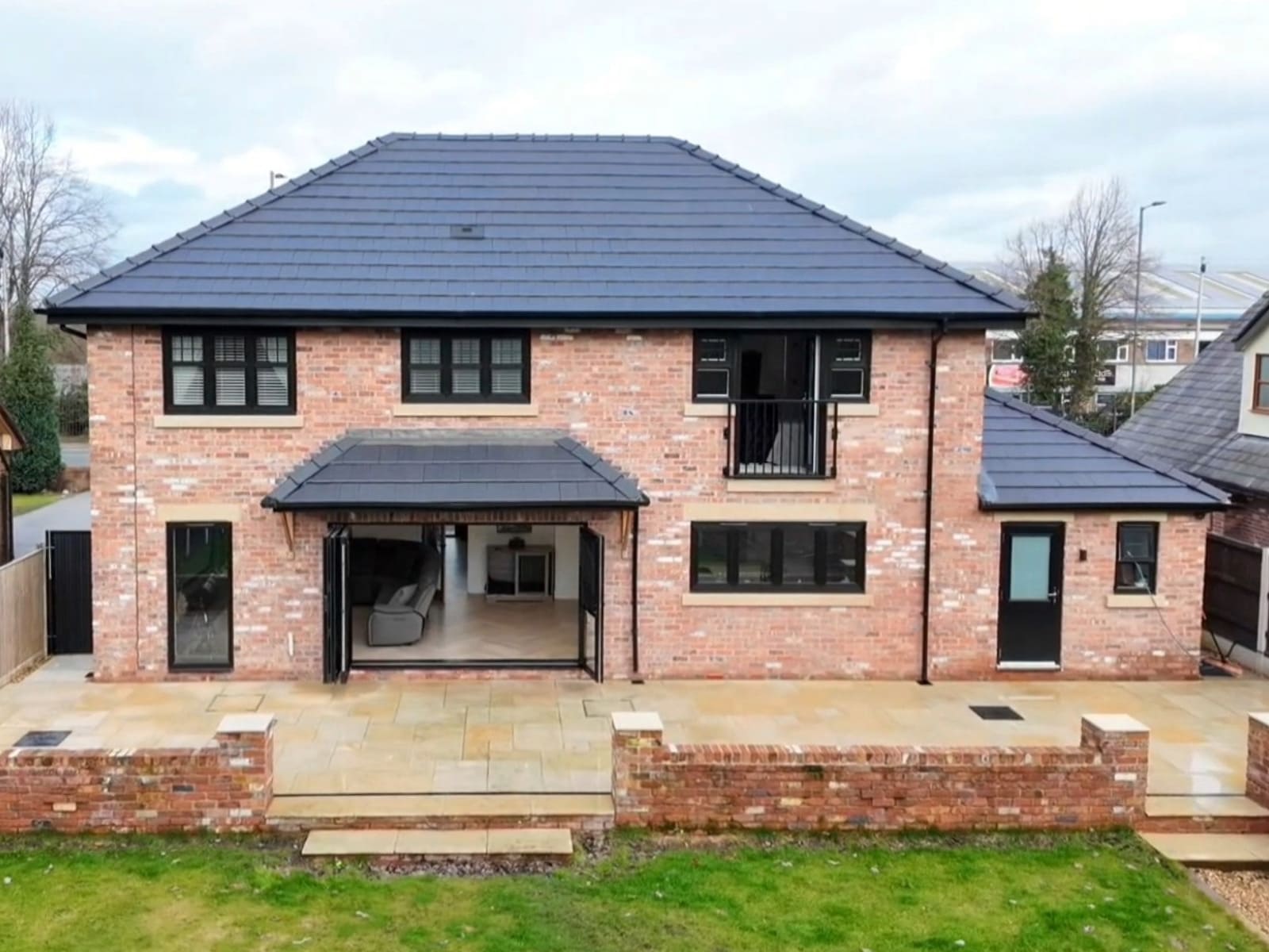 The rear exterior of a large, contemporary two-storey detached house, including an entertainment patio leading down to a spacious garden 